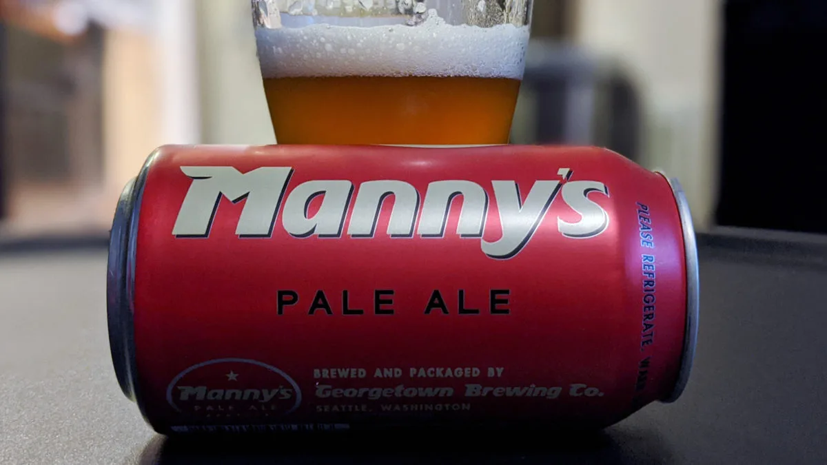 Mannys Can A can of beer laying sideways in front of a glass